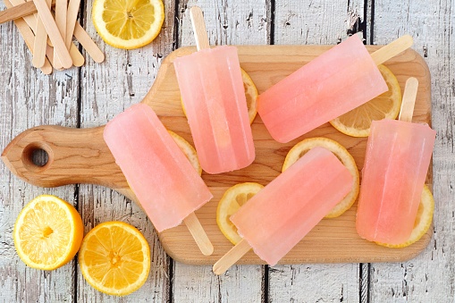 Pink lemonade popsicles with lemon slices on a paddle board with rustic wood background