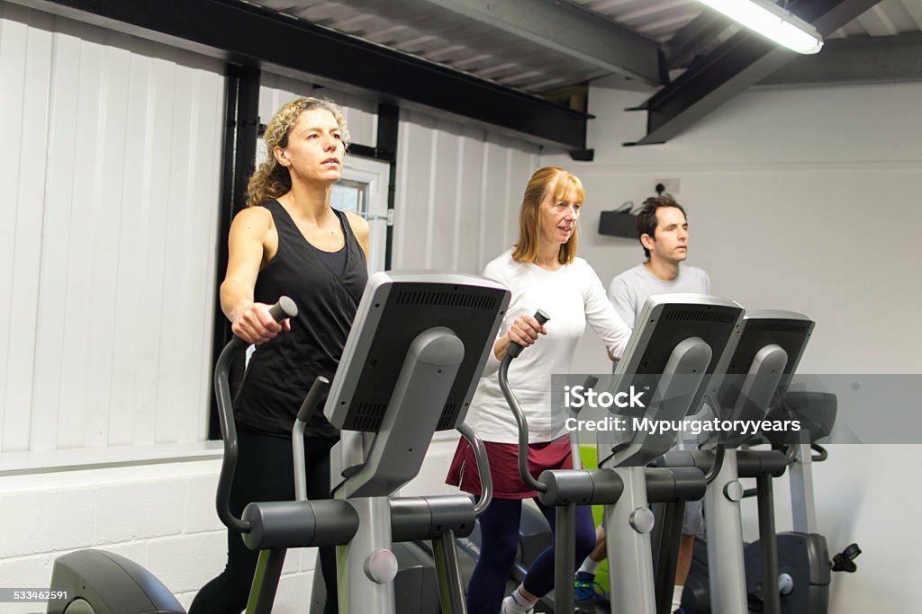 On the cross trainer Three adukts using the cross trainer in a gym 2015 Stock Photo