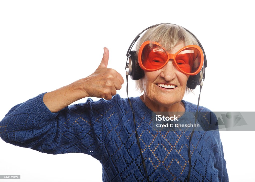 Funny old lady listening music and showing thumbs up. Funny old lady listening music and showing thumbs up. Isolated on white.  2015 Stock Photo