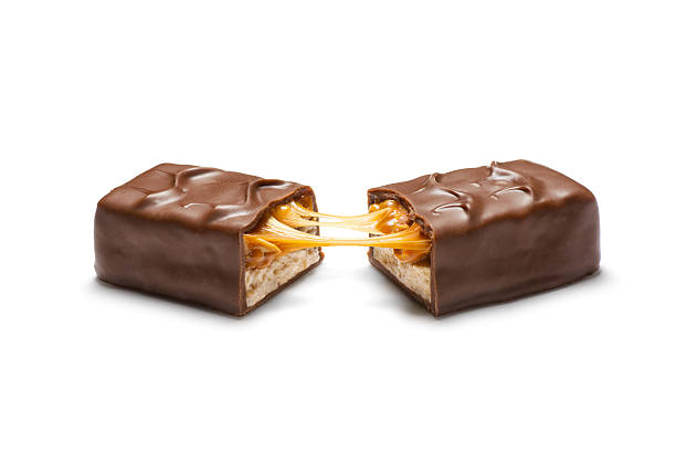 Peanut, Caramel, and Nougat Candy Bar Aspirational style product shot of a common candy bar consisting of peanuts and caramel on a layer of peanut butter nougat, with a chocolate coating.  Candy bar is broken in half and pulled open to reveal interior contents. chocolate bar photos stock pictures, royalty-free photos & images