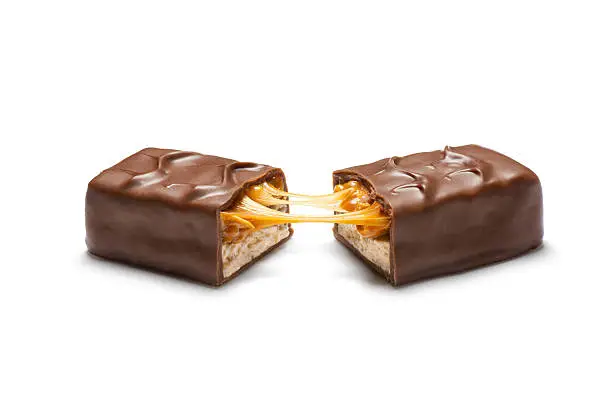 Aspirational style product shot of a common candy bar consisting of peanuts and caramel on a layer of peanut butter nougat, with a chocolate coating.  Candy bar is broken in half and pulled open to reveal interior contents.