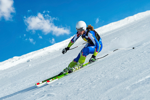 Side view of young female skier at straight downhill race, speed about 100 km/h