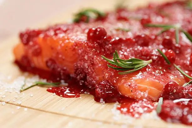 Salmon steak being marinated in salt with rosemary and redberries