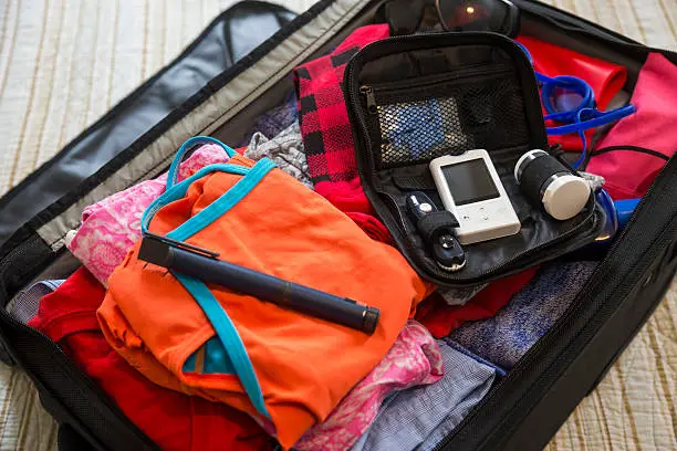 A suitcase with diabetes medical test devices on a bed.  Travelling with diabetes.