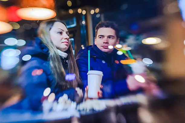 Young tourists, couple, man and woman, drinks coffe in cafe in Manhattan. View trough the window. High ISO, noise, LensBaby photo with selective focus, with reflections.