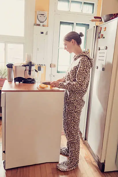 Young woman in onesie using a juicer in small kitchen. Vertical.