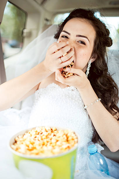 Wedding portrait of bride greedily eating popcorn in car stock photo