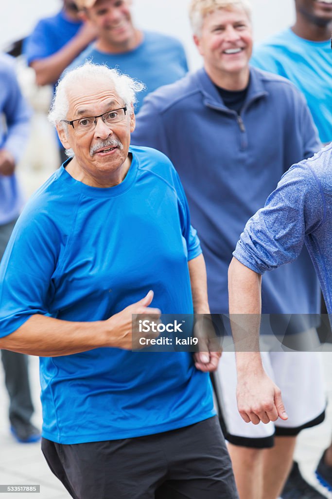 Hispanic senior man running with group Multi-ethnic group of men wearing blue shirts, running together.  Focus is on a senior Hispanic man in his late 70s, wearing eyeglasses. 2015 Stock Photo