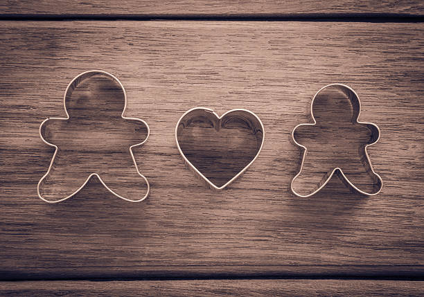 Dolls and heart shape of cookie cutters place on wood background with vignette, retro and sepia tone image, happy wedding anniversary and valentine's day symbol