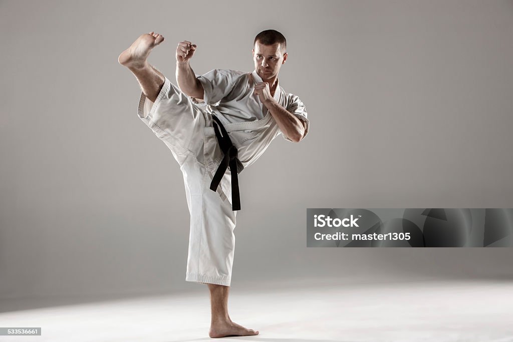 Man in white kimono training karate Man in white kimono and black belt training karate over gray background. 2015 Stock Photo