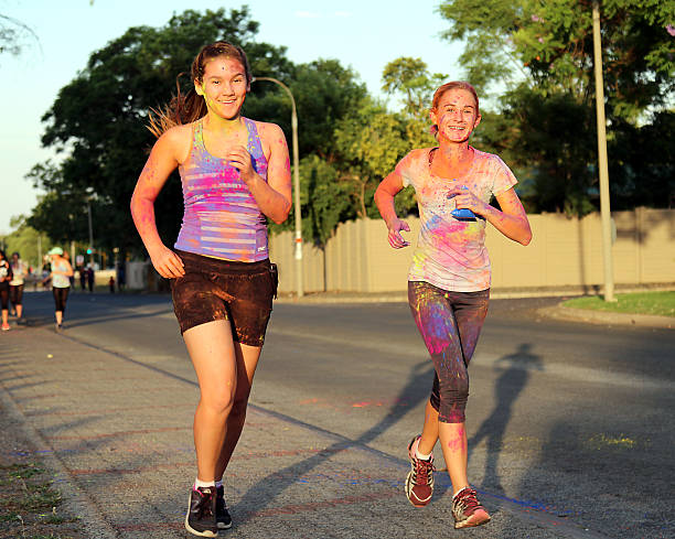 duas adolescentes meninas chearful corrida cobertos com pigmento de tinta - chearful - fotografias e filmes do acervo