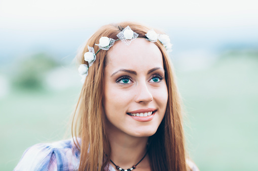 Close up of beautiful young woman with long hair and wreath. Wears checkered shirt and necklace. Looking up.