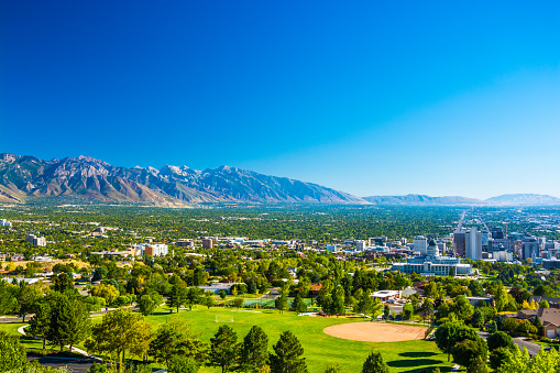 Salt Lake City aerial skyline view with a park in the foreground, downtown to the right, and the Wasatch Range mountain range far in the distance.