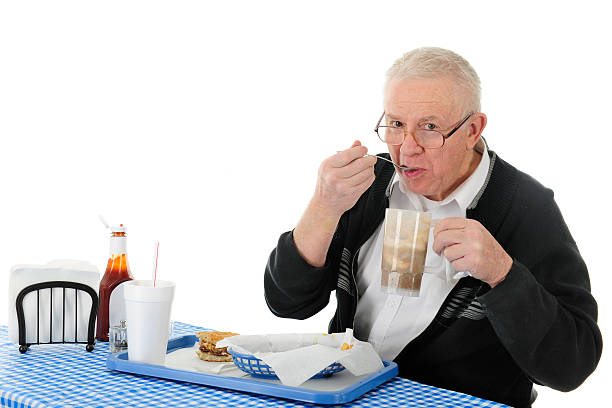 A senior adult man enjoying a meal of hamburger, fries, and a rootbeer float.  On a white background with space for your text over his drink and the ketchup.