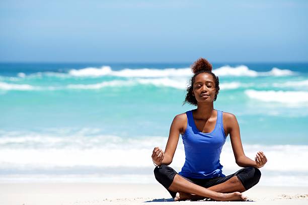 mulher africana jovem meditando em pose de ioga na praia - zen like nature breathing exercise sitting imagens e fotografias de stock