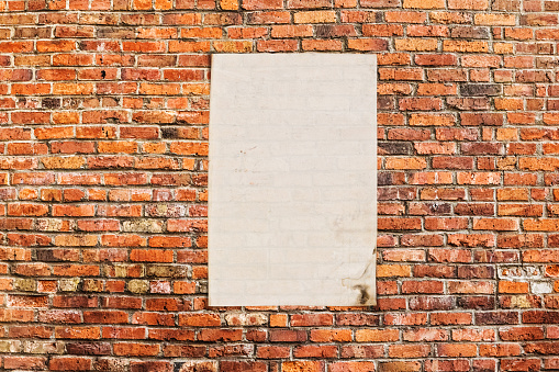 Photo of a grungy red brick wall with a parchment poster stuck to it