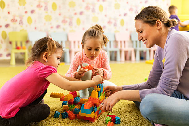 professor e meninas brincando com blocos de brinquedo no jardim da infância. - craft block togetherness community - fotografias e filmes do acervo