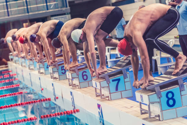 Swimmers crouching on starting block ready to jump Large group of professional male swimmers crouching on their starting blocks, ready to jump into the water at the signal. diving sport stock pictures, royalty-free photos & images