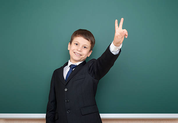 istock school boy in black suit show two finger gesture 533576270