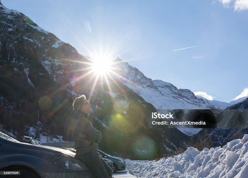 Man leans against car hood below snowy mountains 2015 Stock Photo