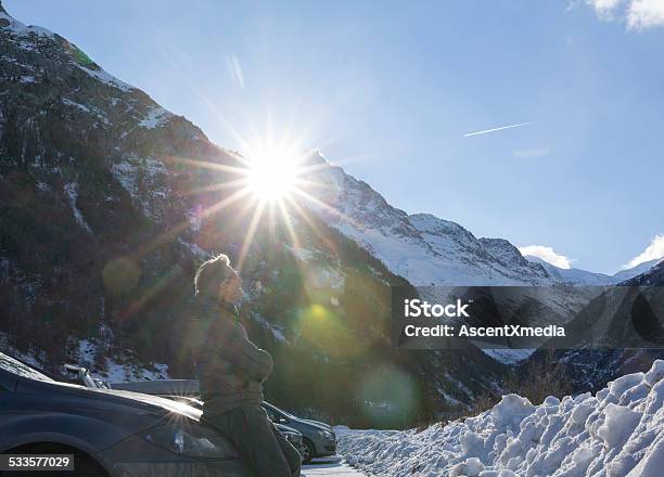 Man Leans Against Car Hood Below Snowy Mountains Stock Photo - Download Image Now - 2015, Above, Adult