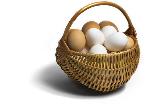 Light  brown wicker basket with colorful fresh eggs on a completely white background with a view angle of 45 degrees.