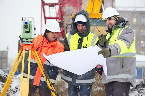 Civil engineers at construction site are inspecting ongoing works according to design drawings in difficult winter conditions
