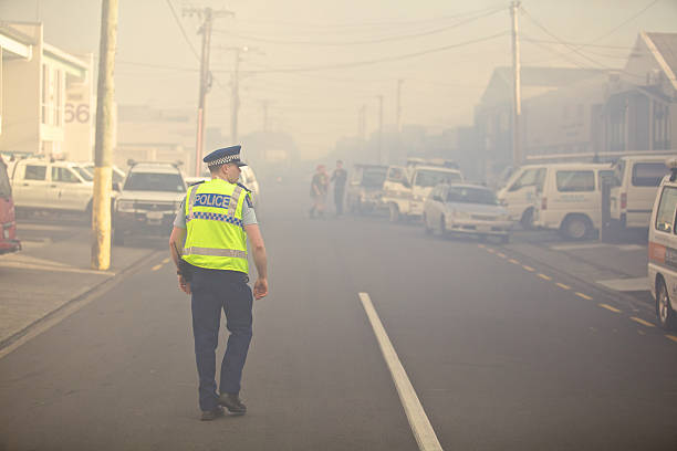 New Zealand Police Officer walks down smokey street during fire stock photo