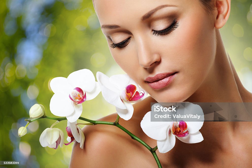 Face of  beautiful woman with a white orchid flower Beauty face of  beautiful woman with a white orchid flower. Skin care treatment. Green nature background Beauty Stock Photo