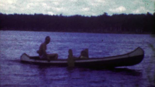 1953: Crafty man driving outboard motor rigged canoe across lake.