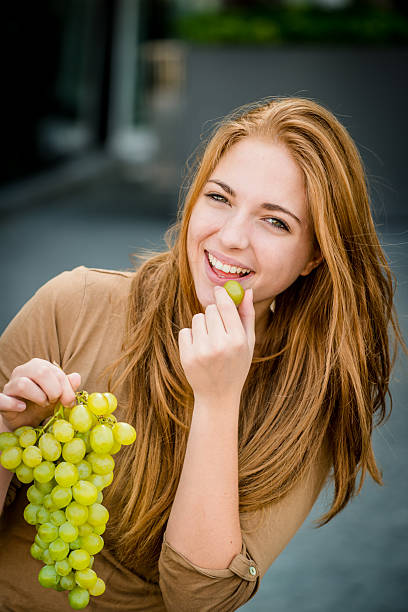 Young woman - teenage girl eating grapes outdoor in street