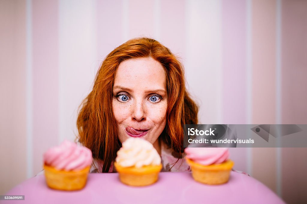 Young Woman Really Wants To Eat Cupcakes Young red head woman really wants to eat pink cupcakes Desire Stock Photo