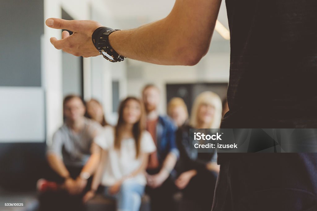 Students on semiar Large group of students sitting in the lecture hall at university and listening to their teacher.  Focus on teacher's hand. Unrecognizable people. Education Training Class Stock Photo