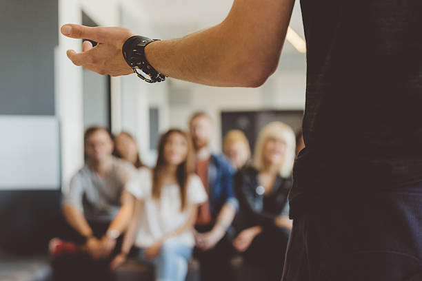 Students on semiar Large group of students sitting in the lecture hall at university and listening to their teacher.  Focus on teacher's hand. Unrecognizable people. lecture hall training classroom presentation stock pictures, royalty-free photos & images