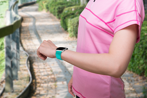 Sport female wearing smartwatch with blank black glass bent touchscreen on natural tree background