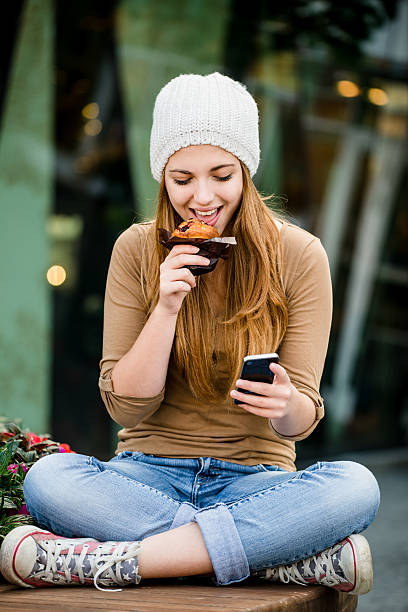 adolescente mangiare muffin alla ricerca del telefono - muffin blueberry muffin blueberry food foto e immagini stock