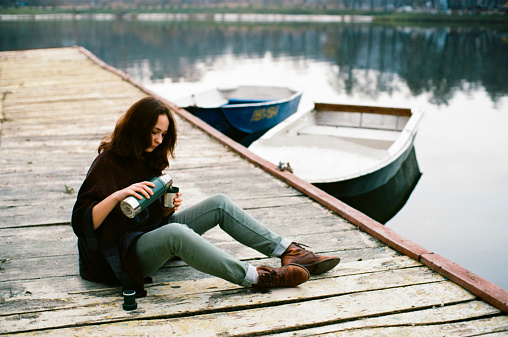 Girl drinking tea sitting on the pier near the lake