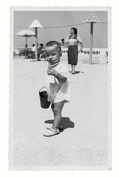Mother and son at the beach in 1950 Mother and son at the beach in 1950. Some skratches and grain due to the age of the photo. Scanned black and white print. parasol photos stock pictures, royalty-free photos & images
