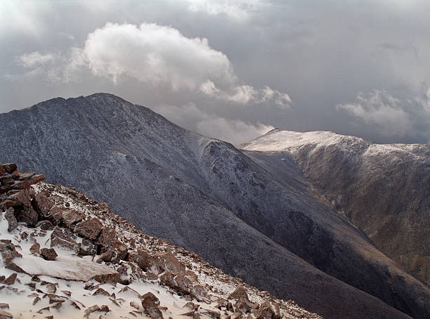 Snow and sleet fall on the rock covered scree slopes of Mount Shavano at 14,236 feet high as one looks from Tabeguache Peak at 14,155 feet. High winds blow storms and clouds over the peaks of the Sawatch Range. 