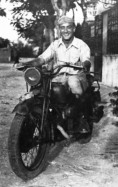 Happy Man on motorbike in 1945. He is stationary in an urban road. Some skratches and grain due to the age of the photo. Scanned black and white print.