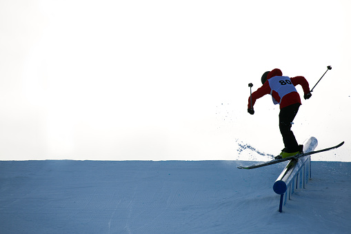 A teenaged male alpine skier does a rail grind during a slope style competition at a winter ski resort.