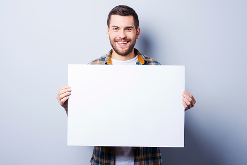Handsome young man holding copy space while standing against grey background