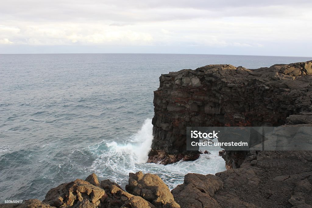 Natural rock arch on the Hawaiian coast Natural volcanic rock arch on the Hawaiian coast formed by the erosion of the waves and tides with surf flowing through and a large wave breaking on the headland Coastline Stock Photo