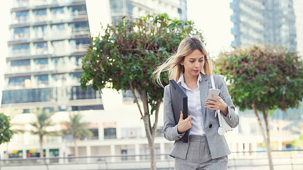 Businesswoman texting in Dubai Color image of a western female expatriate walking while texting with her mobile phone. Letterbox format with copy space left. expatriate photos stock pictures, royalty-free photos & images