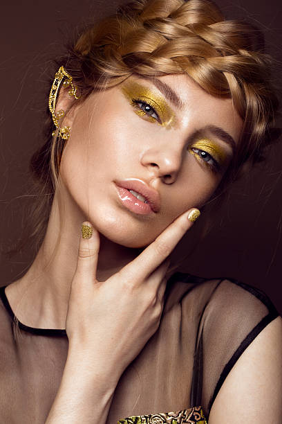 Beautiful girl in gold dress with creative makeup and braids Beautiful girl in a gold dress with creative makeup and braids on her head. The beauty of the face. Photos shot in the studio. blonde model in dress stock pictures, royalty-free photos & images