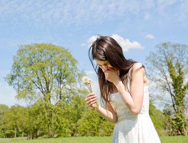 An attractive young woman blowing on a dandelion in an open field