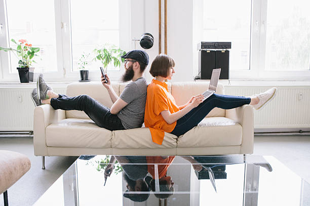 hipster couple sit on couch and look into digital devices