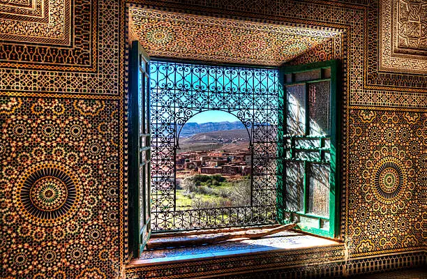 An ornate window in the Kasbah Telouet in Morocco overlooks the fields and Atlas Mountains