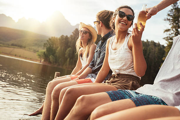 Portrait of young people sitting on a jetty on a sunny day. Happy young men and women enjoying their holiday at the lake.