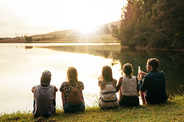 istock Young people sitting in a row by a lake 533703242